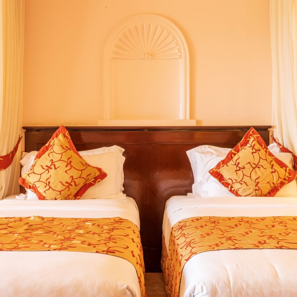 Two elegant twin beds with decorative pillows and curtains at Lake Victoria Serena Golf Resort & Spa in Kampala.