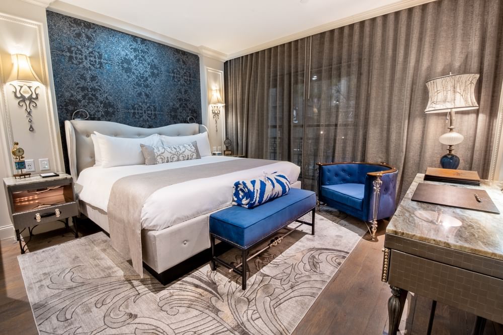 A hotel room with a king-sized bed, blue accents, and a large window.