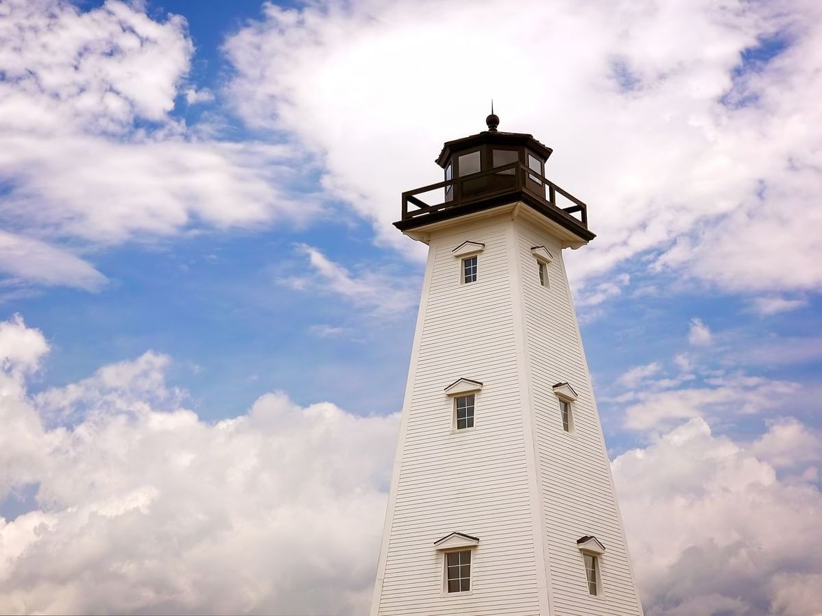 A tall, white wooden lighthouse with dark trim stands against a bright, cloudy sky in Jones Park near The Markham Hotel
