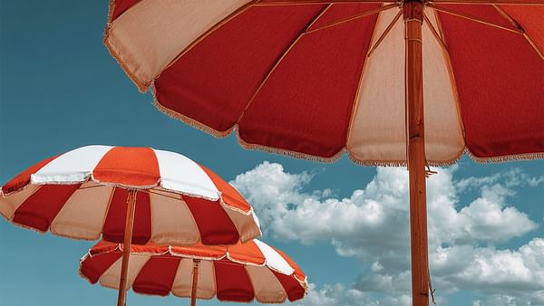 Three red and white beach umbrellas against a blue sky with white clouds.