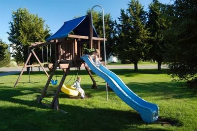 Wooden playground set with a slide and a swing, surrounded by green grass at Breezeway Boutique Hotel