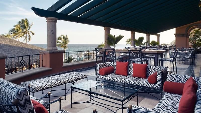 Lounge patio with black-and-white patterned sofas overlooking the ocean at Bar Santo Al Reves in Hacienda del Mar Los Cabos