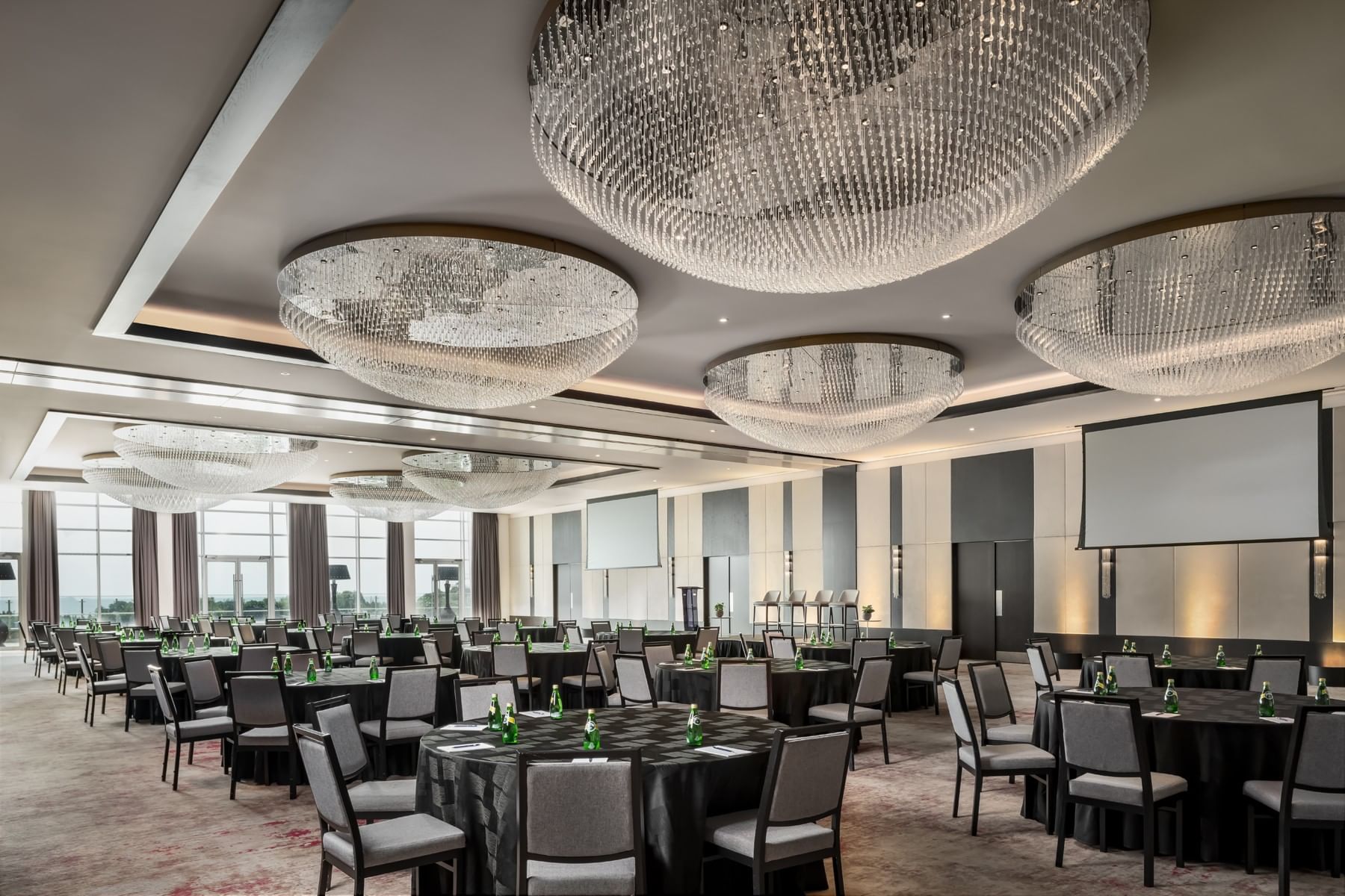 Victory Ballroom with gray chairs set in rows under oval crystal chandeliers by tall windows at Hotel X Toronto