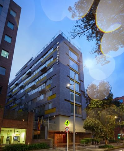 Edificio hotelero de múltiples pisos, con árboles y señalización de tránsito en la calle.