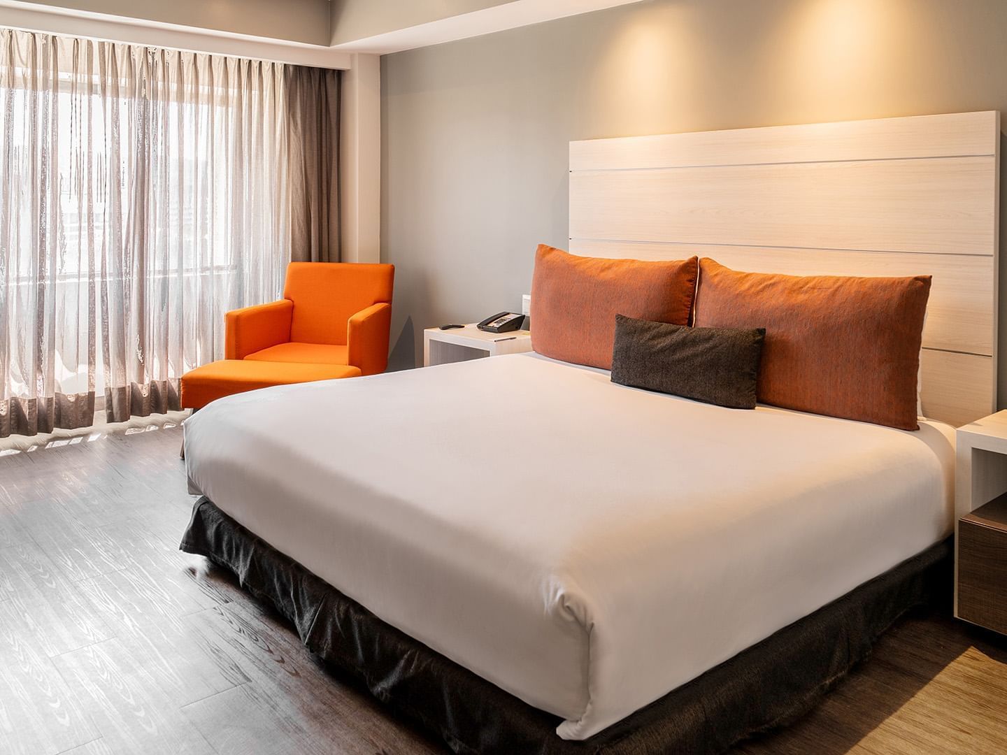 Cozy lounge chair and nightstands by the bed in the King Executive Room with wooden floors at Real Inn Tijuana