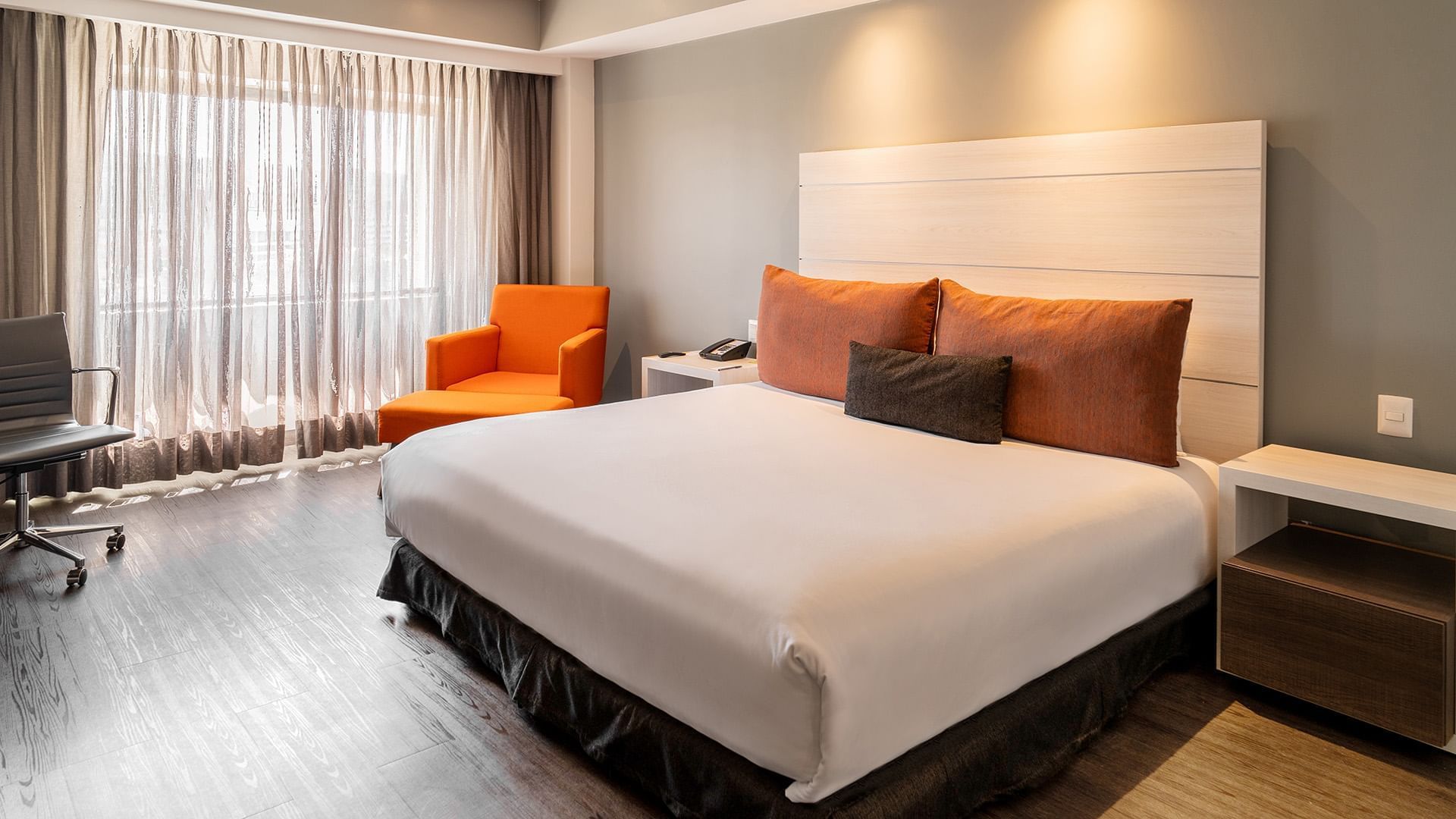Cozy lounge chair and nightstands by the bed in the King Executive Room with wooden floors at Real Inn Tijuana