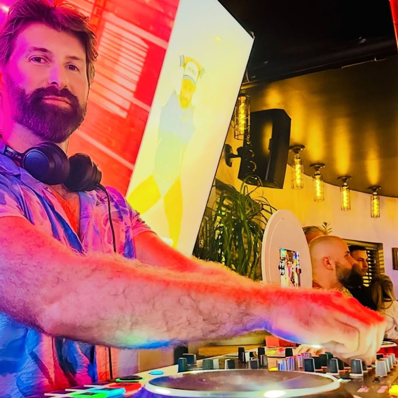 A DJ performs live with colorful lighting and vibrant visuals in a lively bar, engaged with the audience at The Gaythering