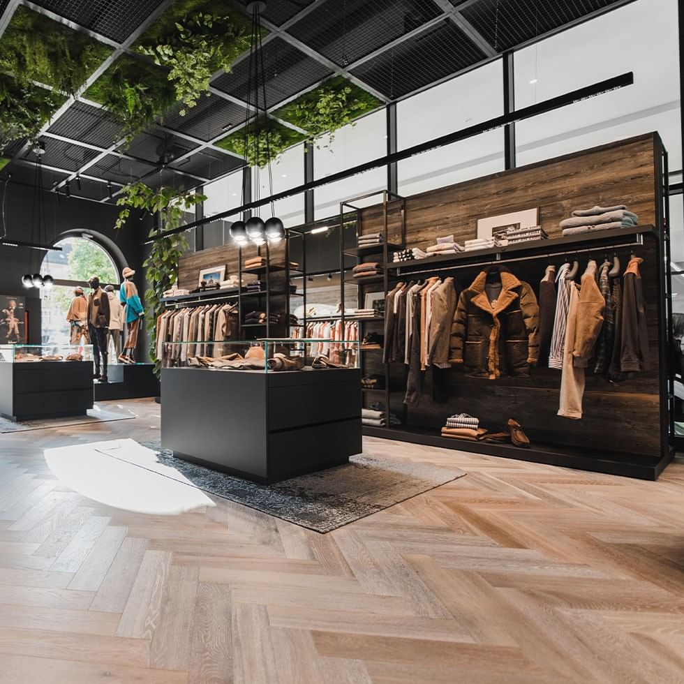A modern boutique store with wooden floors, hanging plants, and glass displays.