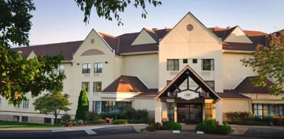 Exterior front entrance of a multi-story hotel with a peaked roof and tan facade at Branson Hillside Hotel on a sunny day