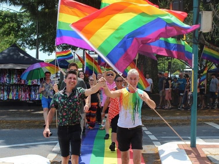 People crossing the road smiling and waving rainbow-coloured flags