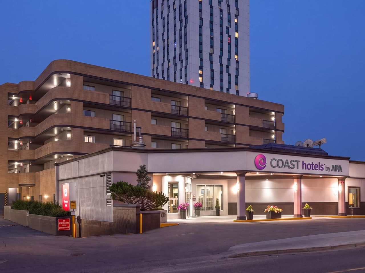Illuminated exterior view of a modern multi-story hotel building at dusk with prominent entrance and signage