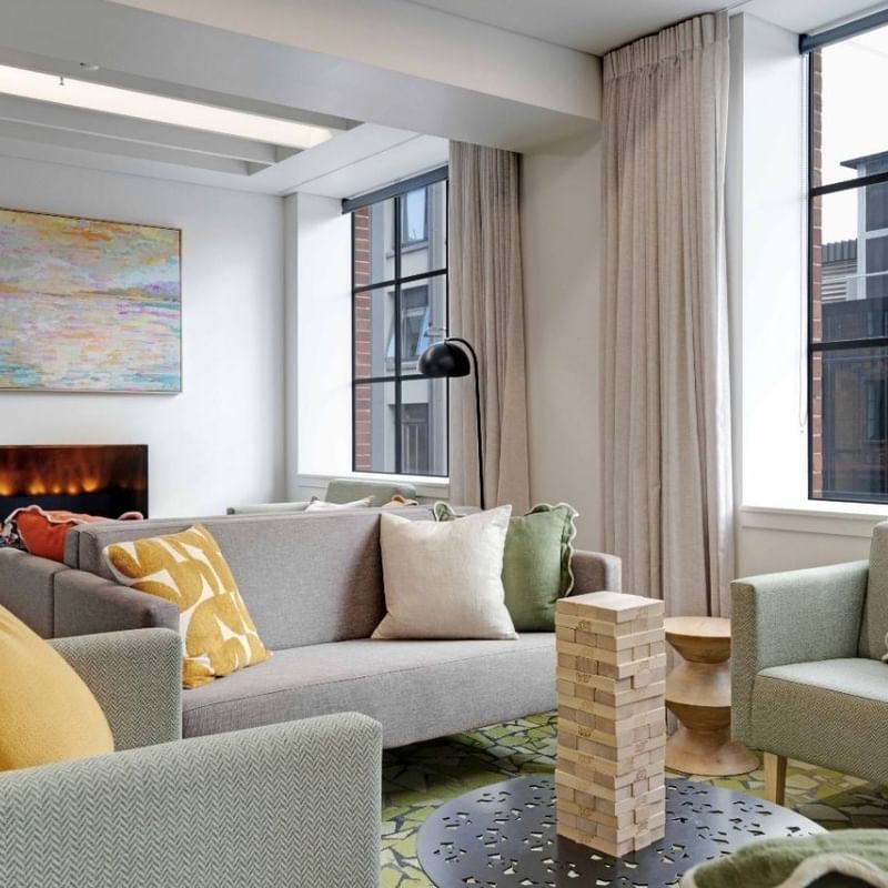 Modern communal lounge with gray sofas, colorful cushions, electric fireplace, and large windows at UniLodge Auckland Central