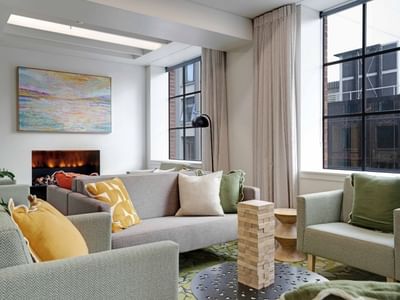 Modern communal lounge with gray sofas, colorful cushions, electric fireplace, and large windows at UniLodge Auckland Central