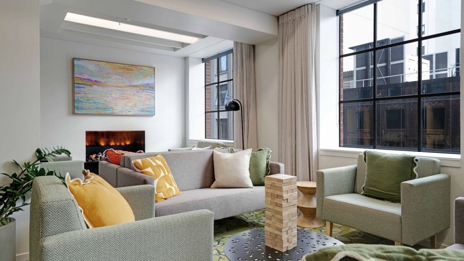Modern communal lounge with gray sofas, colorful cushions, electric fireplace, and large windows at UniLodge Auckland Central