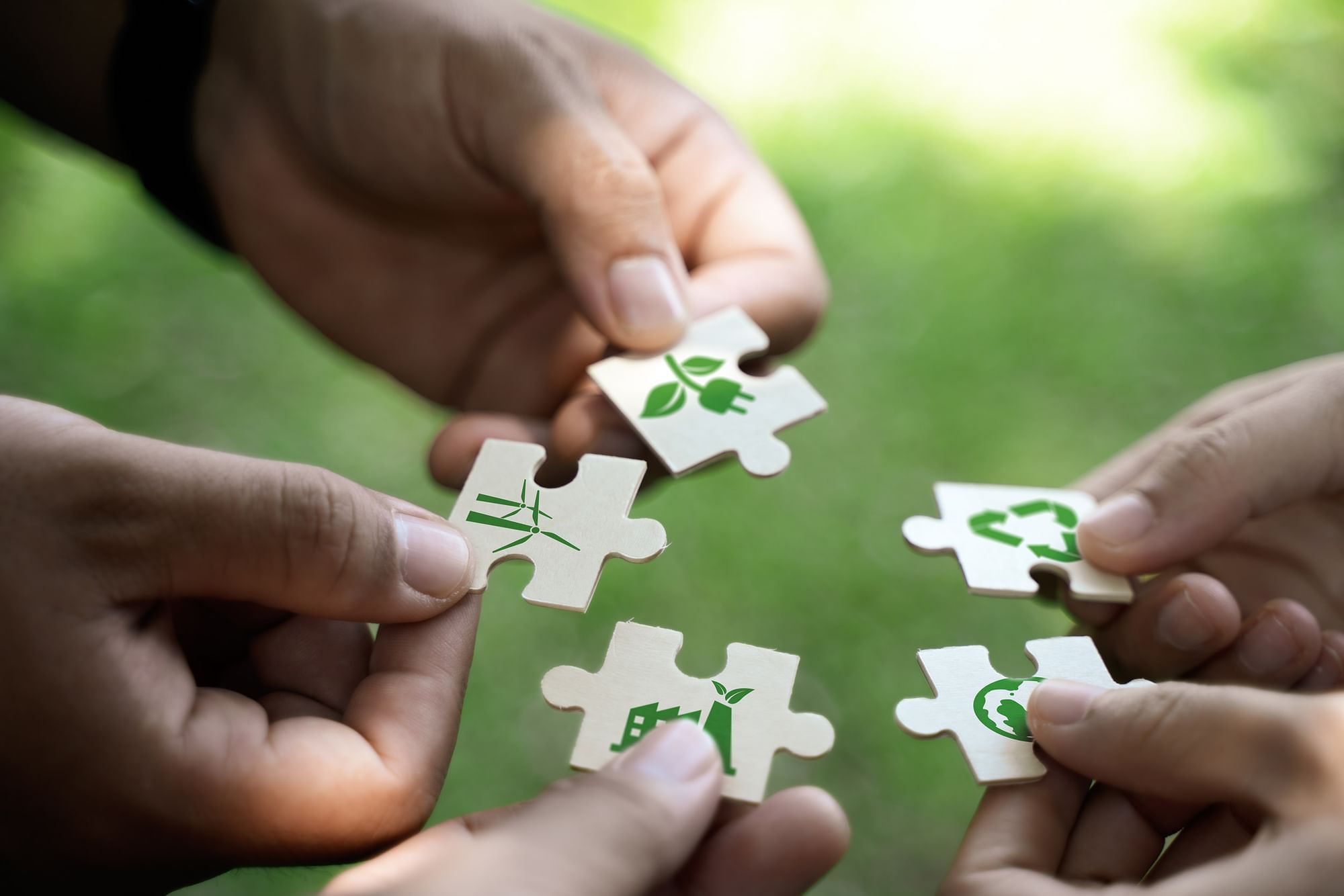 Four hands holding puzzle pieces with green environmental icons at Warwick Hotels and Resorts