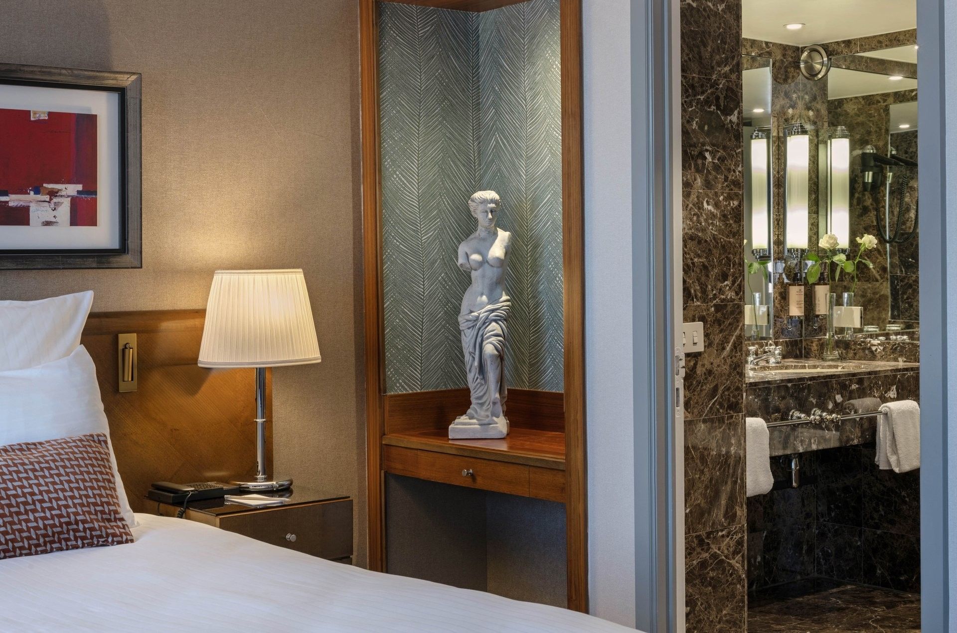 Warwick Suite with a lamp placed by a statue on a wooden stand at Warwick Grand Place Brussels