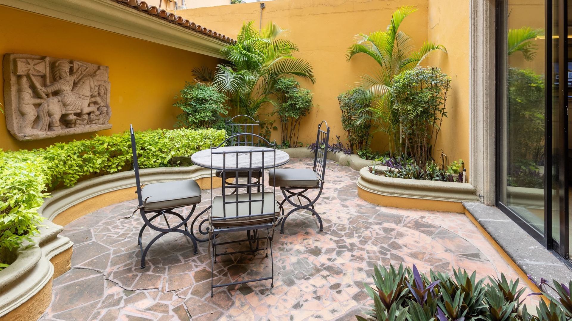 Terraza privada con mesa de hierro forjado, sillas y plantas tropicales en Quinta Real Monterrey.