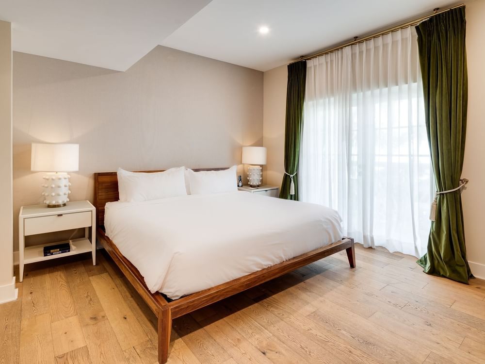 A neatly made bed with white linens and pillows in a room with light wood floors and beige walls.