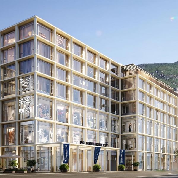 Exterior view of Falkensteiner Hotel Bozen WaltherPark facade featuring glass windows with a mountain backdrop