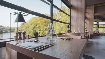 A restaurant interior with a large window, showcasing the outdoors, and a table set with cutlery.