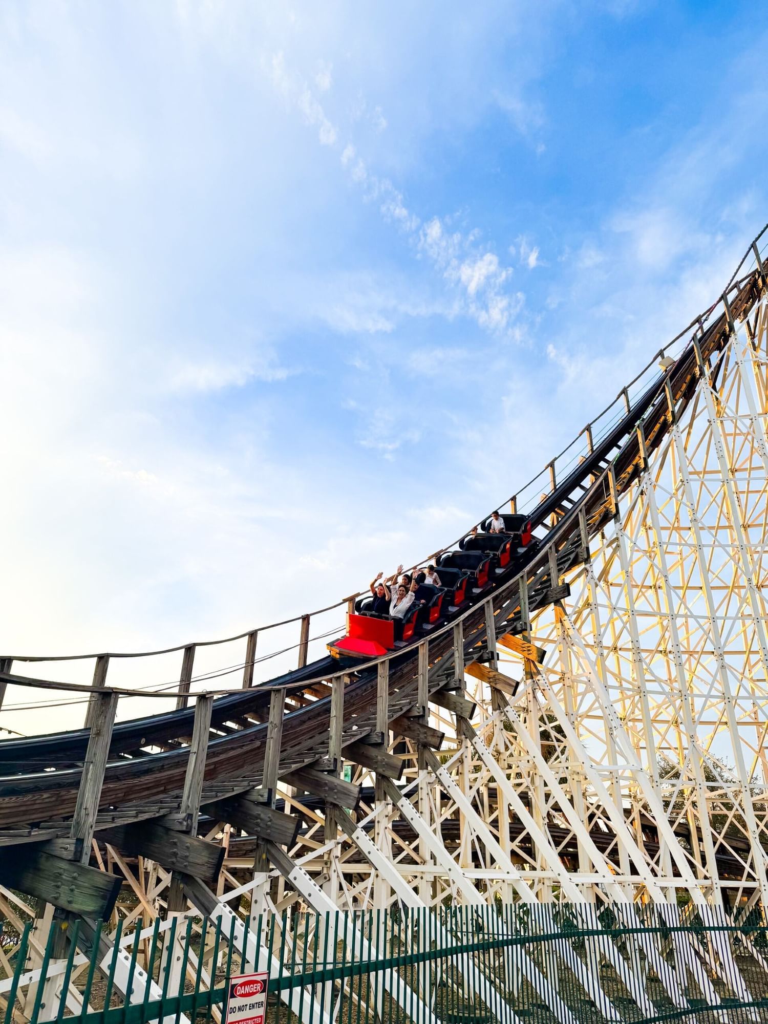 A car full of riders on a roller coaster zooming down a track against a sunset sky. 