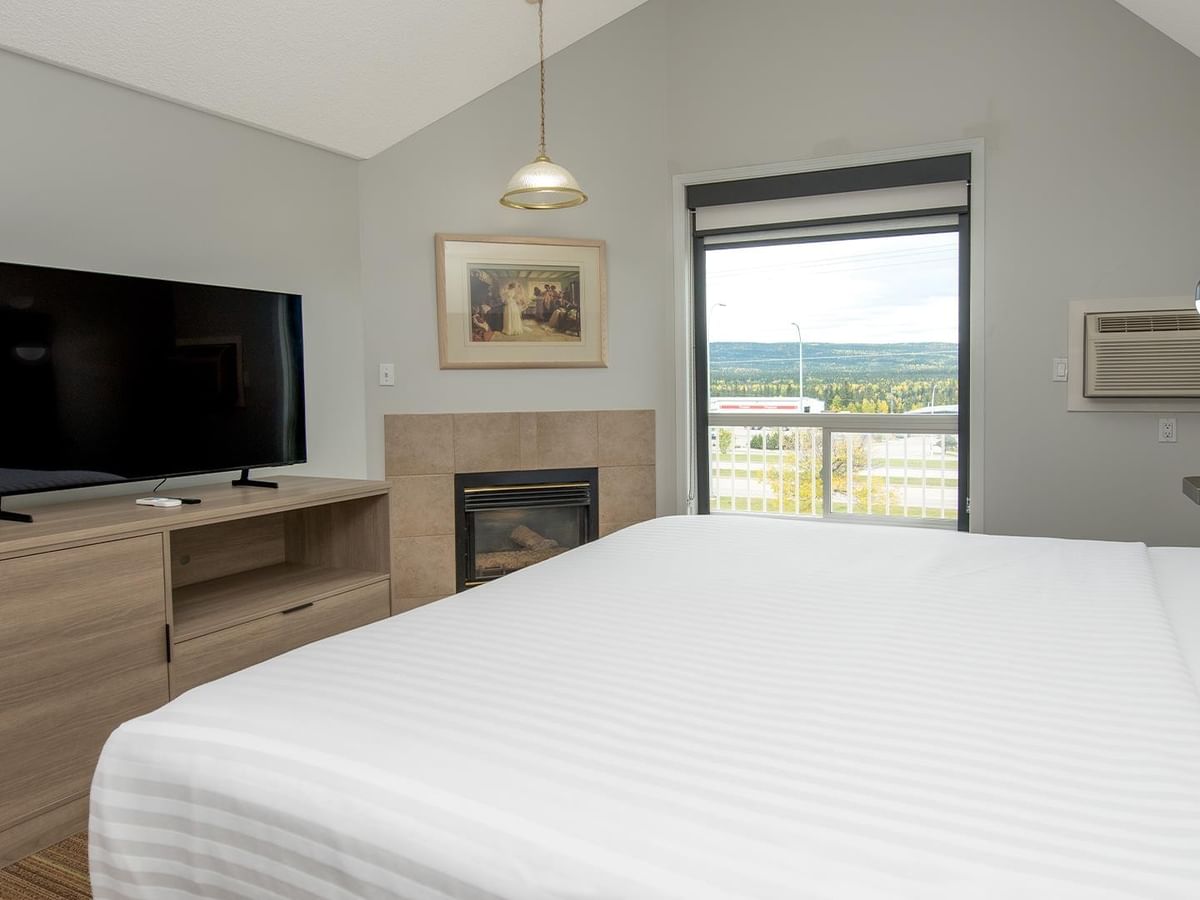 Coast Suite with white bedding, fireplace, flat-screen TV, and scenic window view.