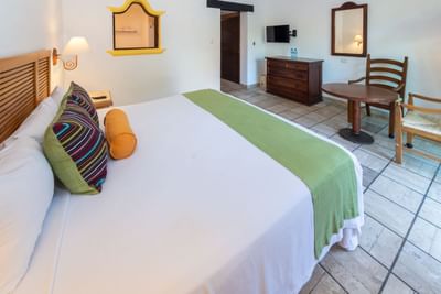 A bedroom with a large bed, colorful pillows, wooden furniture, and a TV mounted on the wall.