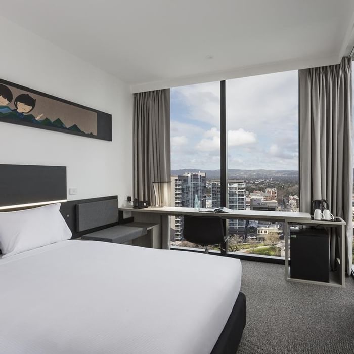 Bed and workspace by the large window offering city views in the Superior Room One Queen Bed at Ibis Adelaide
