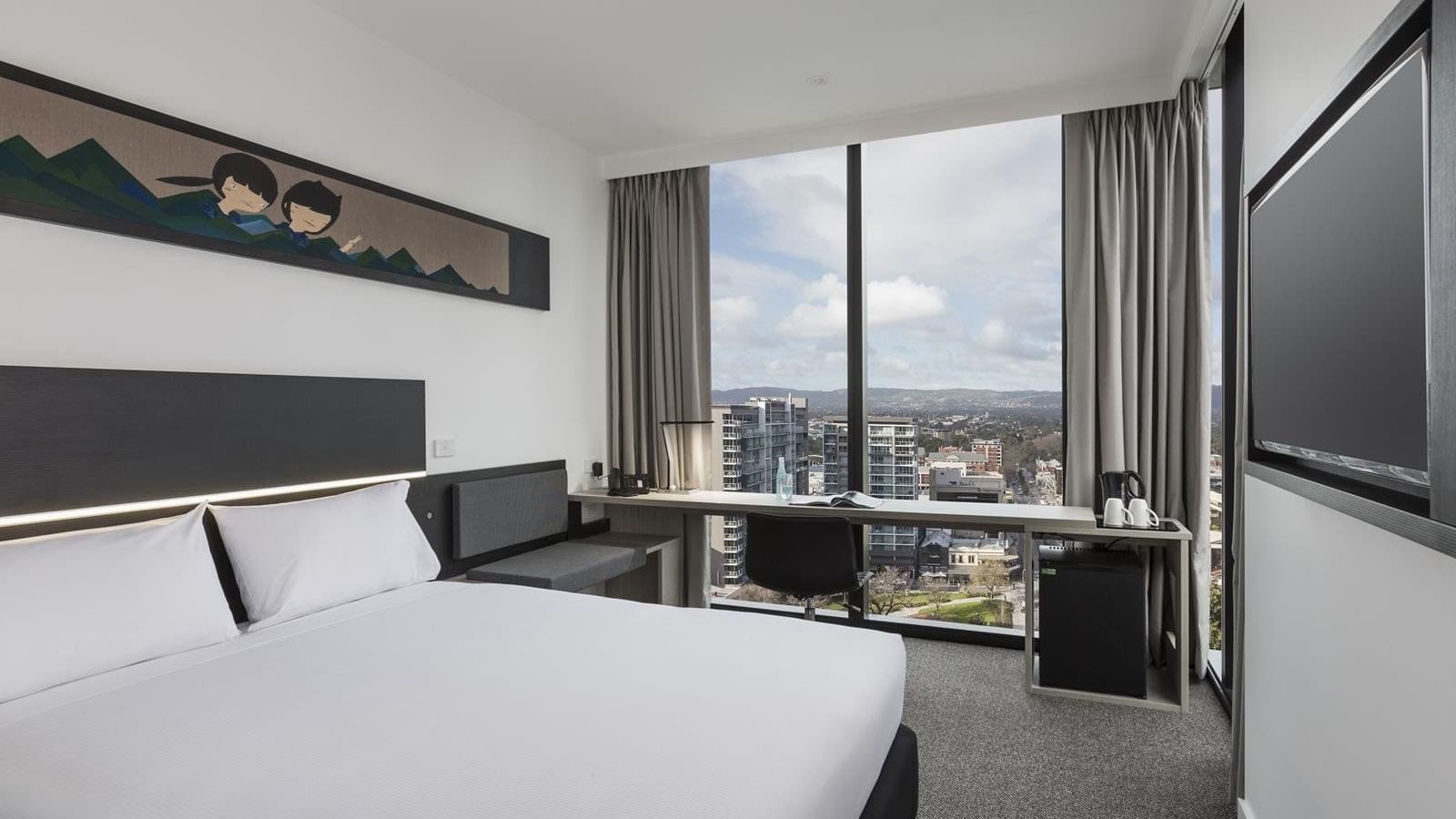 Bed and workspace by the large window offering city views in the Superior Room One Queen Bed at Ibis Adelaide