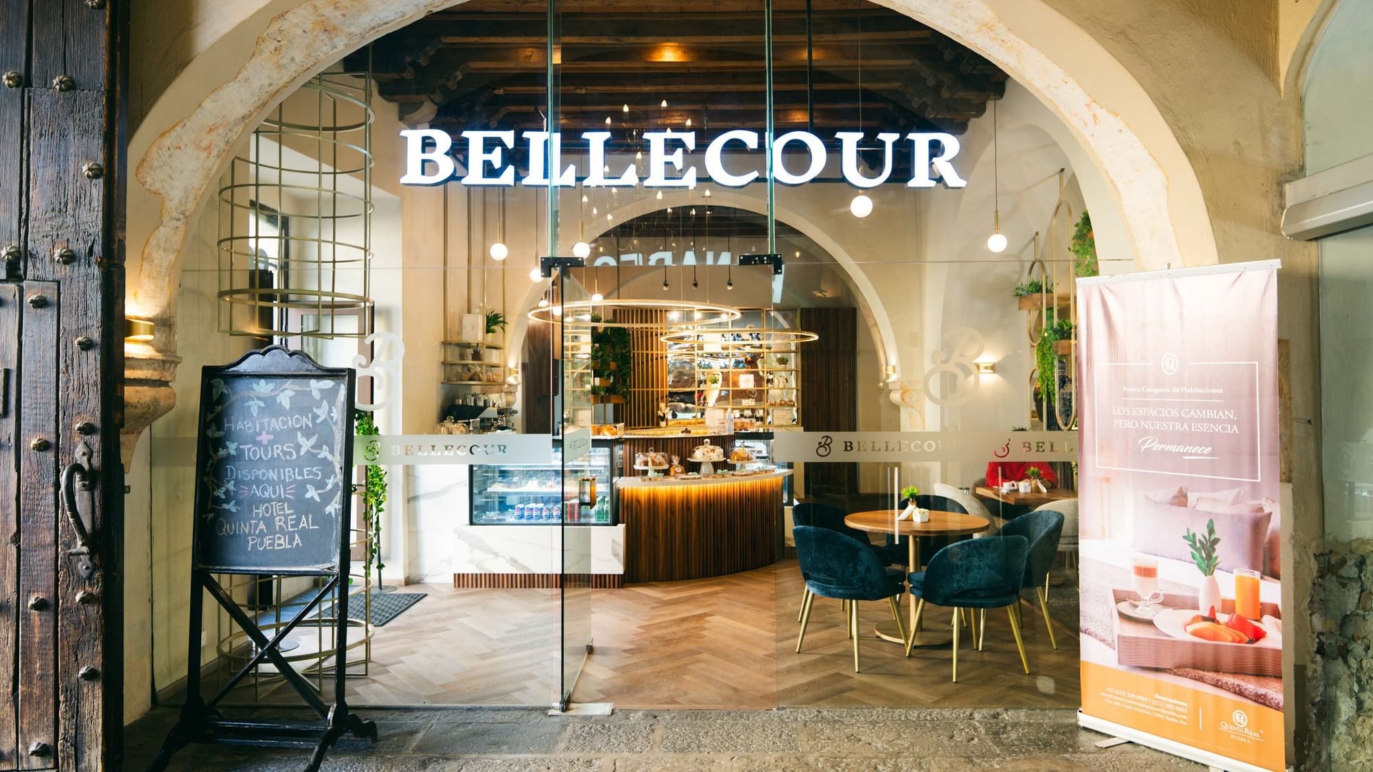 Entrada a café Bellecour a través de arco de piedra con sillas de terciopelo azul en Quinta Real Puebla