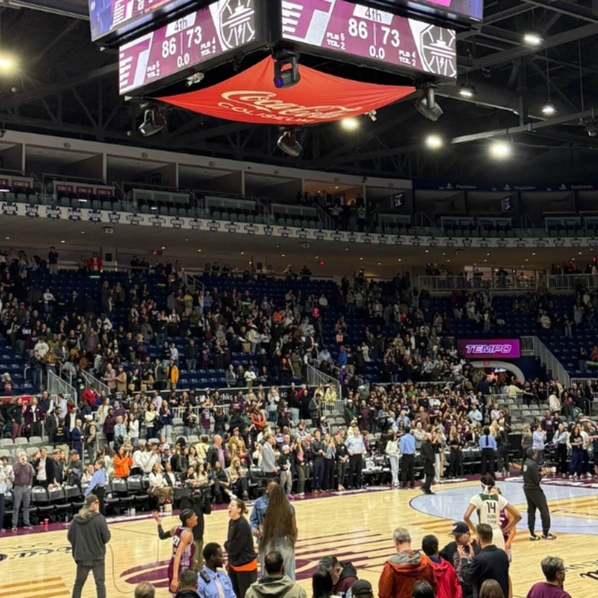 Basketball players by crowded stands under a hanging scoreboard during a game at Coca-Cola Coliseum near Hotel X Toronto