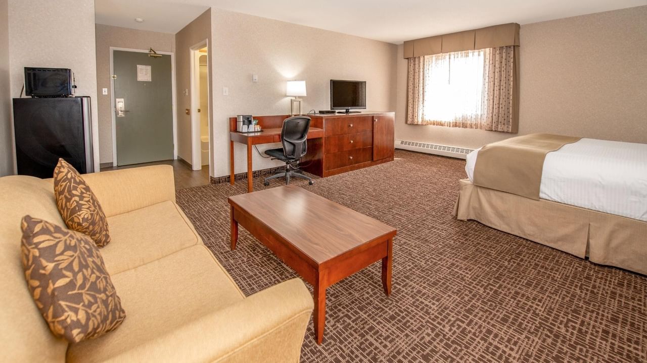 Hotel room with a couch, coffee table, desk, chair, TV, and a bed.