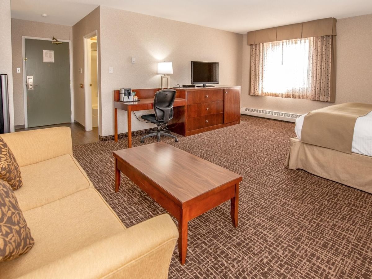 Hotel room with couch, coffee table, desk, chair, TV, and a bed.