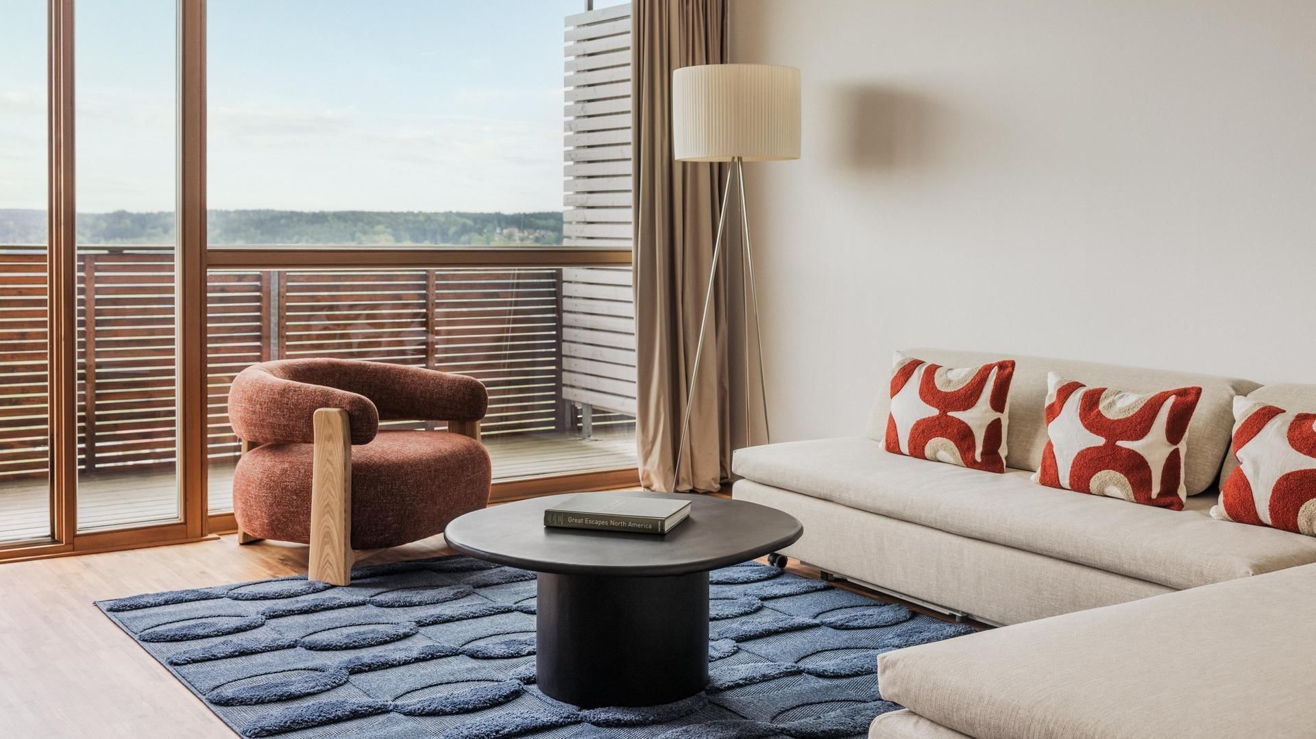 Living room with couch, patterned pillows, round coffee table, chair, and floor lamp by large window.