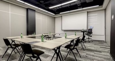 Modern conference room with arranged tables, green bottled water, and a projector screen in Rooms E F & G at Hotel Nodo