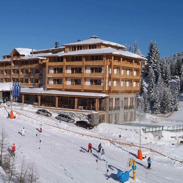 Falkensteiner Hotel Cristallo Katschberg beside a snowy ski slope with skiers and pine trees