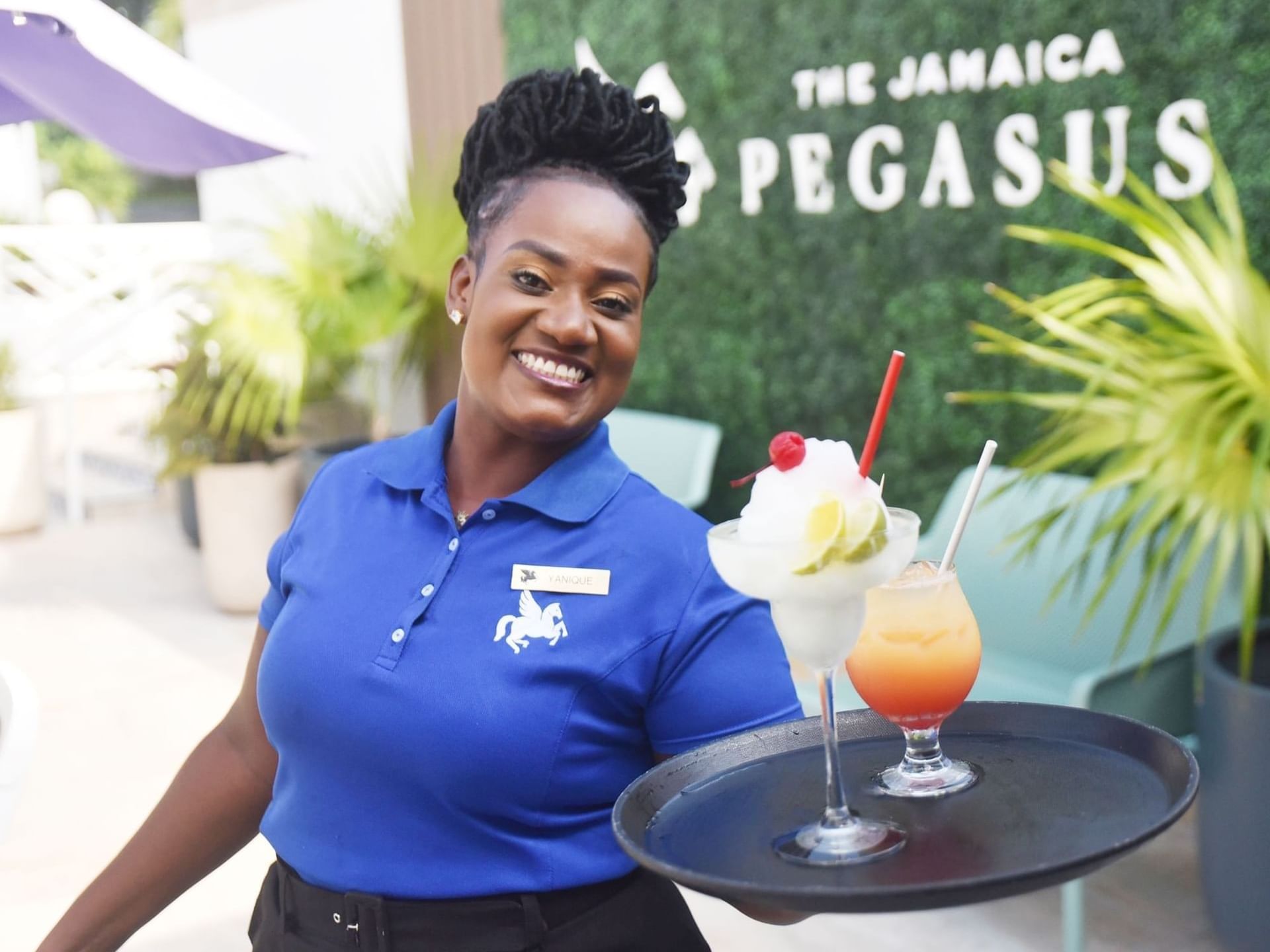 Server in a blue polo holding a tray with frozen cocktails near the garden wall at the Jamaica Pegasus Hotel