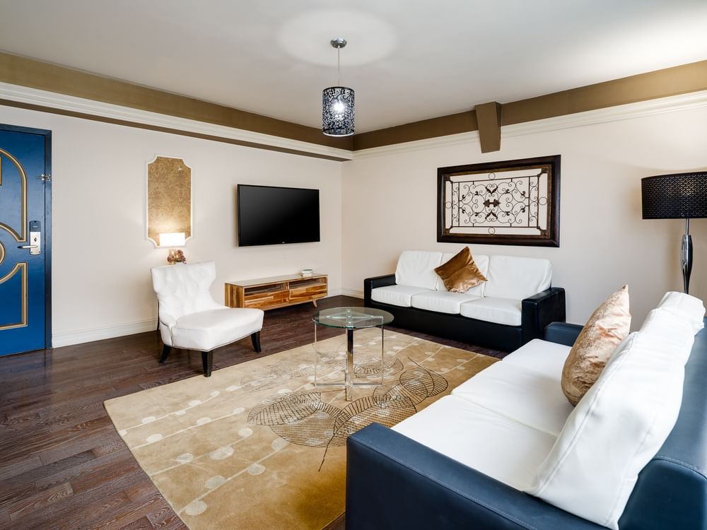A wide-angle view of a hotel room's living area with a sofa, armchair, coffee table, and TV.