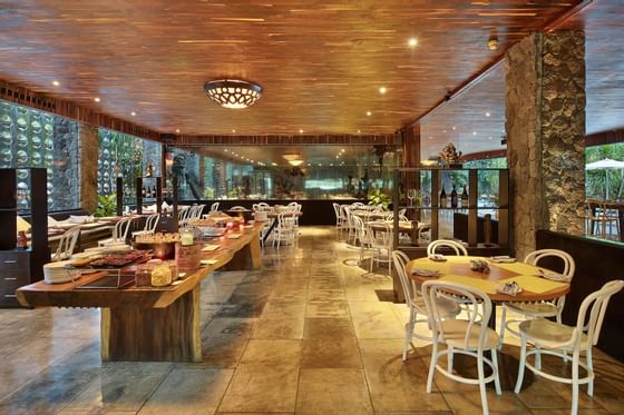 Dining area with wooden tables and white chairs under a wooden ceiling at Peppers Seminyak
