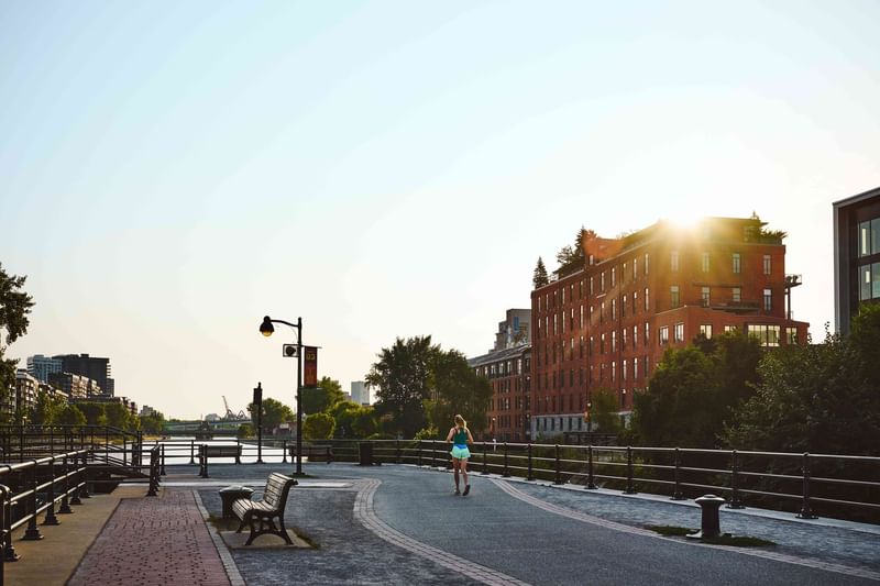 Woman jogging on waterfront path with red brick buildings and canal at sunset at Warwick Le Crystal Montreal