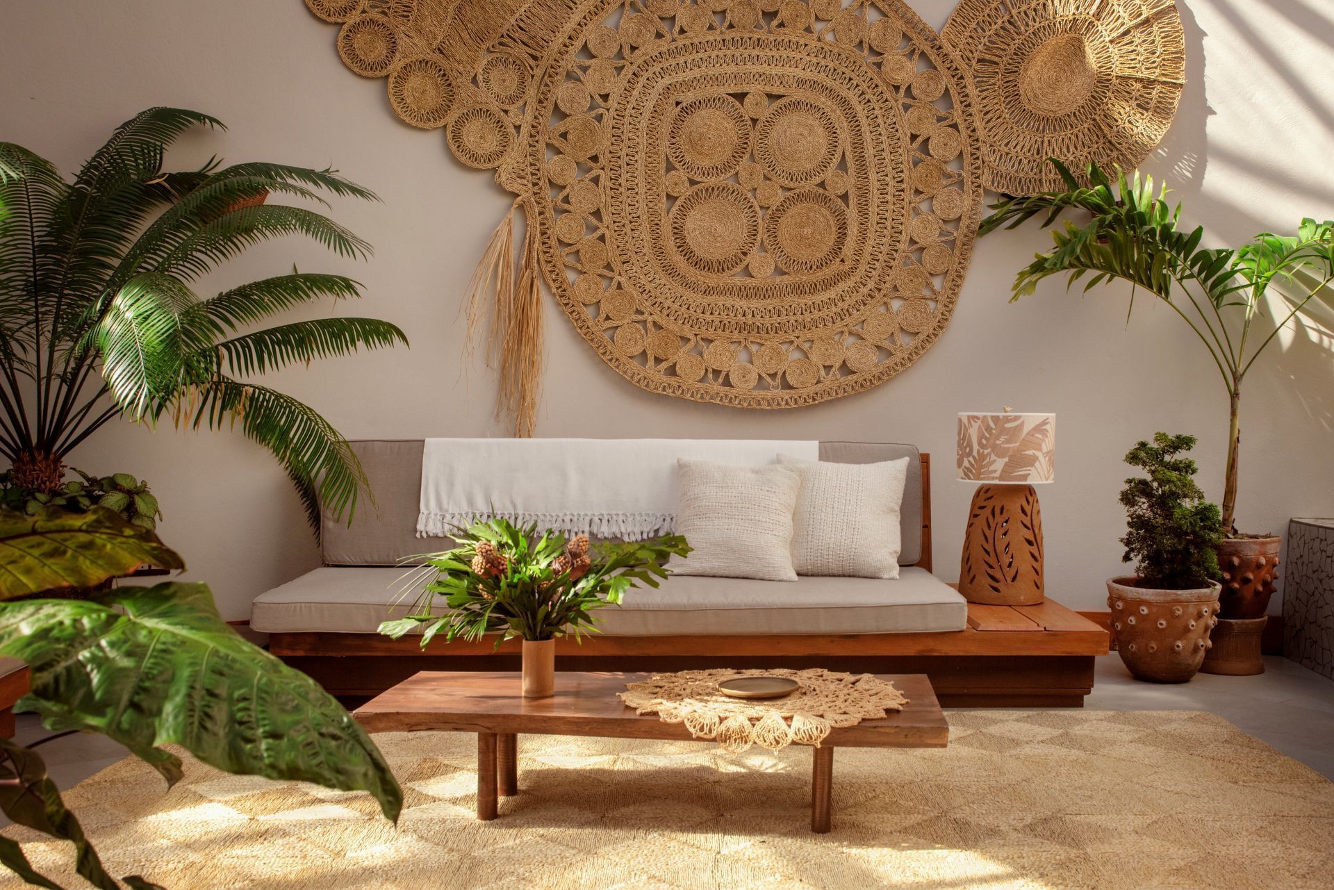 A tropical living room with couch, coffee table, wall art, and various plants.
