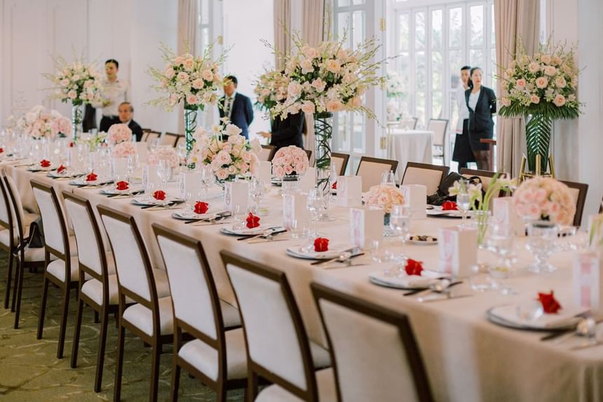 An elegantly arranged dining table adorned with pink floral centerpieces, glassware, and rose petals at Park Hyatt Saigon
