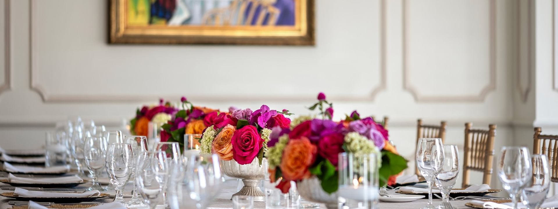 Floral centerpieces on a table by crystal glasses under a classic painting in The Bridewell Suite at Warwick Melrose Dallas