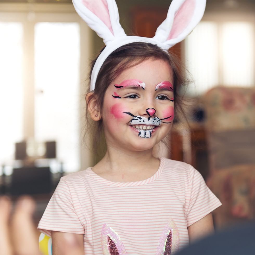 Bambina con trucco facciale da coniglio e orecchie di coniglio per Pasqua in montagna.