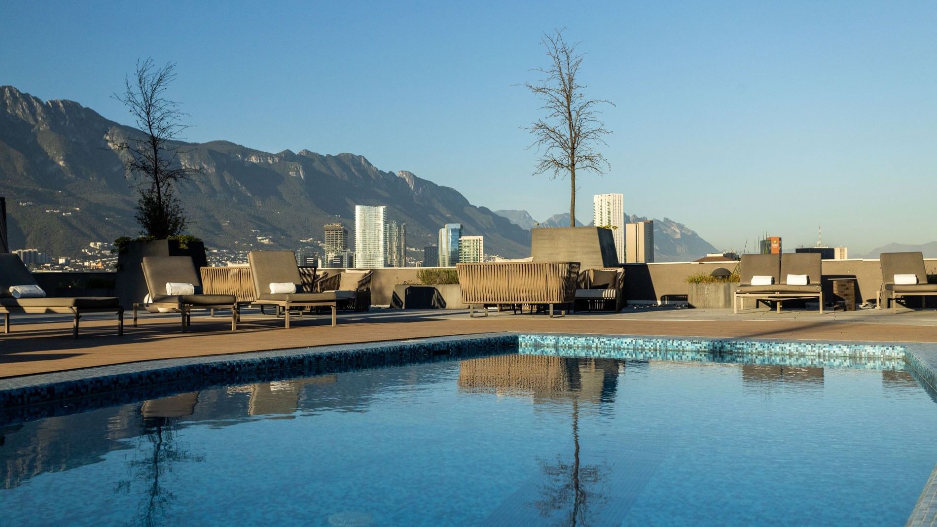 Sparkling rooftop swimming pool with lounge chairs and mountain range views at Camino Real Fashion Drive, Monterrey
