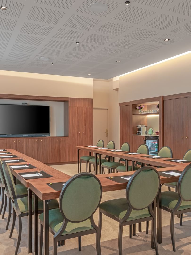 U-shaped table with green cushioned chairs & a wall-mounted TV in the Westminster meeting room at Warwick Reine Astrid - Lyon