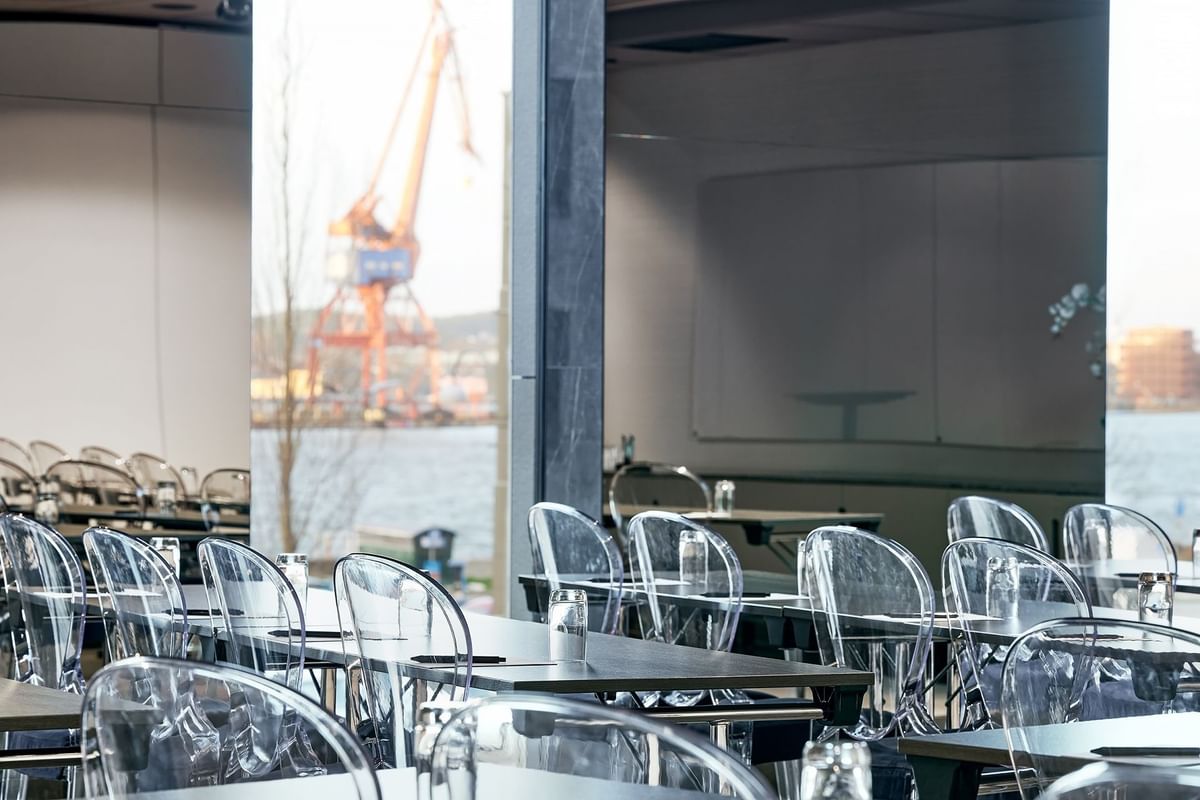 Mötesrum med glasbord och stolar, vattenglas på varje bord, och utsikt över hamnen med en kran.