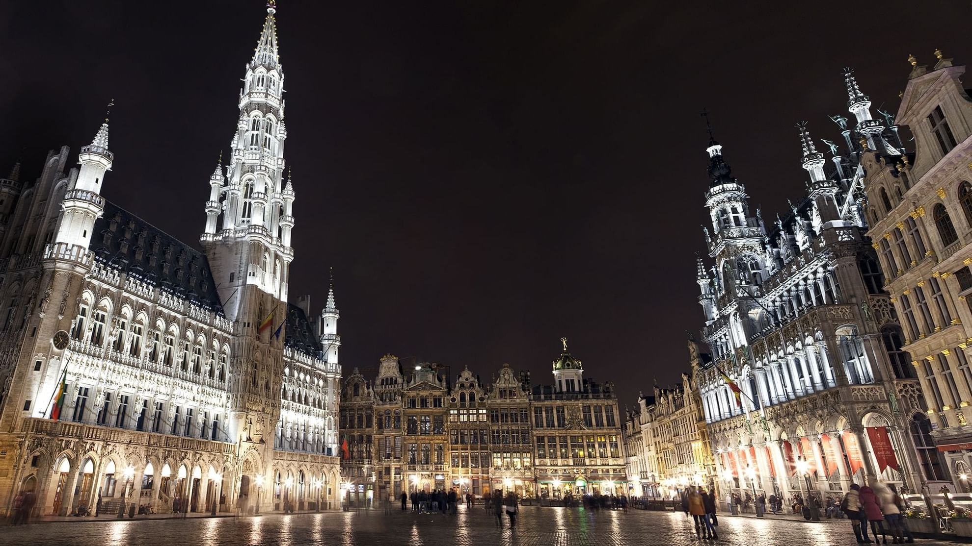 Illuminated historic buildings surround a cobblestone square at night in Brussels, near Warwick Hotels and Resorts