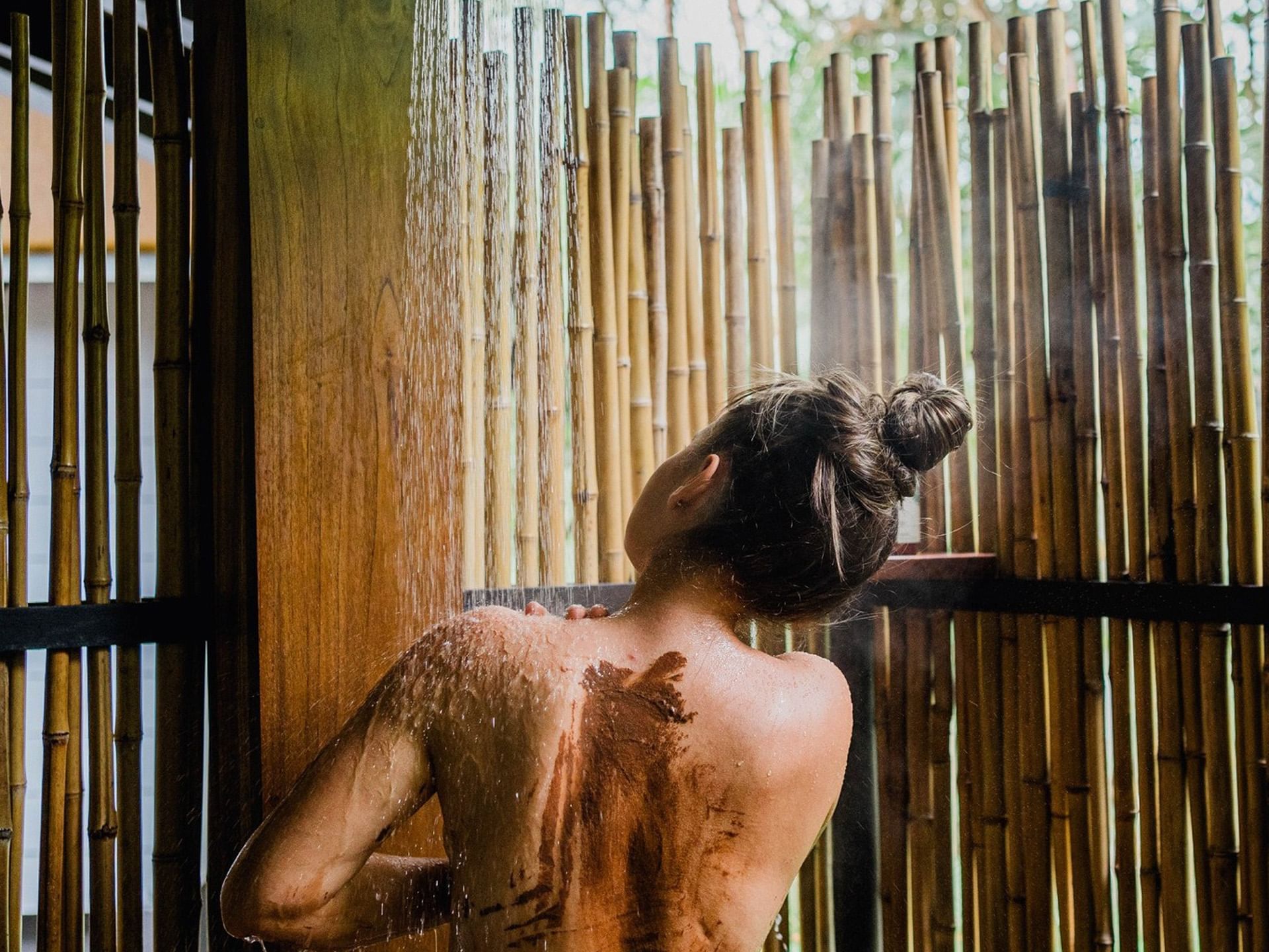 Lady enjoying an outdoor shower surrounded by bamboo walls in Esencia Spa at El Silencio Lodge and Spa