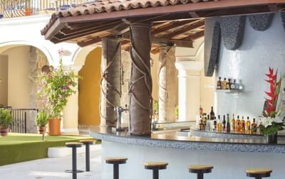 Outdoor poolside bar with mosaic tile counter, wrapped columns, and tropical flowers at Playa Los Arcos Puerto Vallarta 2023